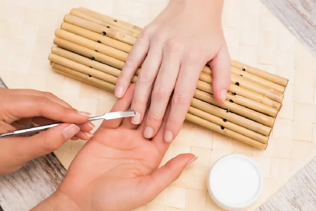 Nail technician gently pushing back a client's cuticles with a metal tool during a manicure